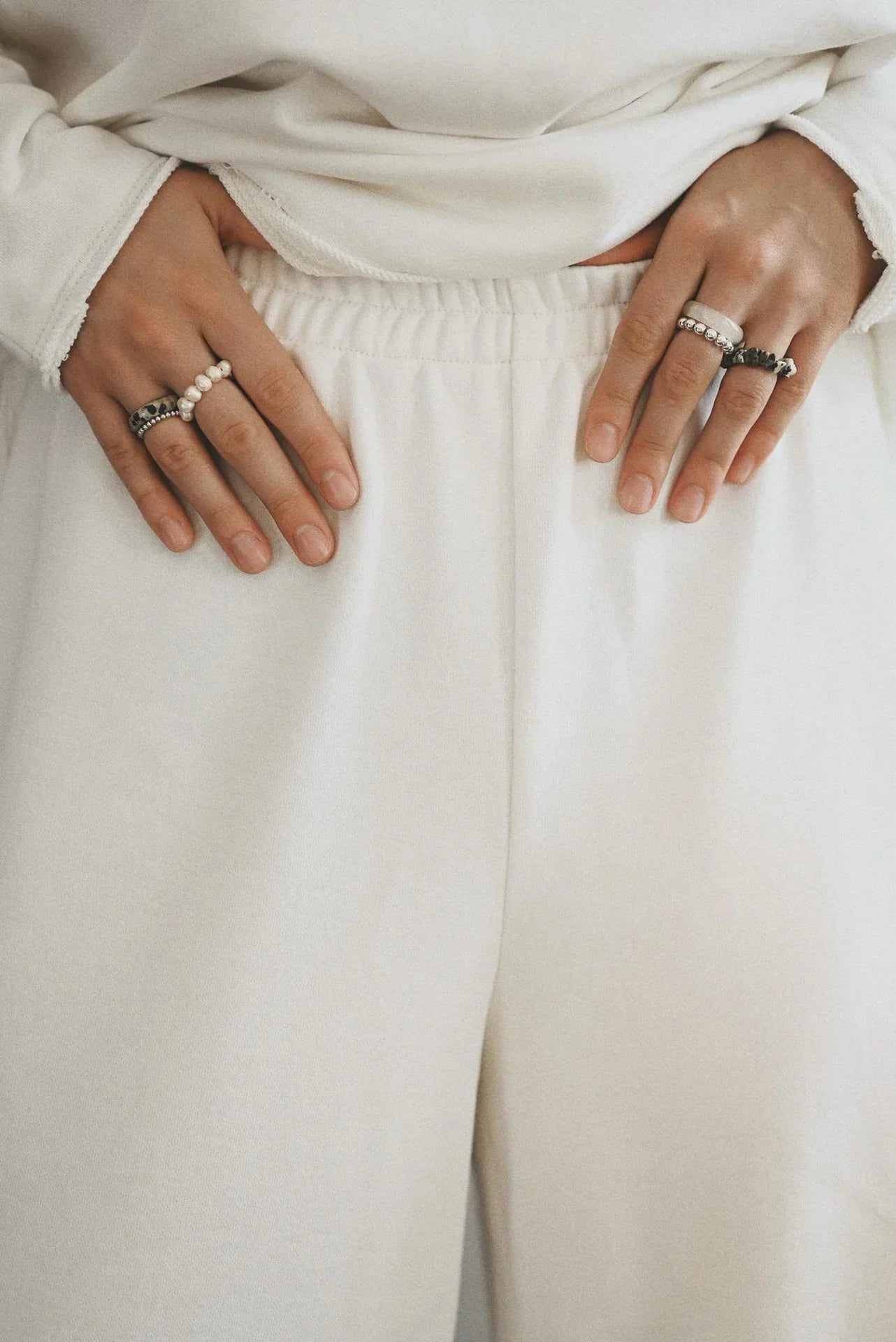 Close-up of a person wearing a white outfit, with their hands resting on their waist, adorned with multiple rings.